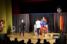 Na zdjęciu widać przedstawienie na scenie. Cztery osoby — jedna kobieta i trzech mężczyzn — występują przed publicznością. Na scenie znajduje się także bęben oraz skrzynka, a także rekwizyty takie jak krzesło, drewniane palety i dyskotekowa kula. Zdjęcie przedstawia występ kabaretu Hrabi.