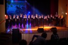 Na scenie grupa dzieci występujących. Ubrani na czarno z białym dodatkiem na szyi i maską na głowie.
