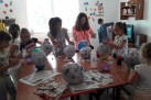 Dzieci tworzące dzieło z balonów, na które naklejają gazetę. Pracują przy jednym stole.