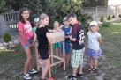 Na zdjęciu grupka dzieci pracująca nad drewniana budowlą. Jeden z chłopców trzyma w dłoniach wiertarkę akumulatorową. 