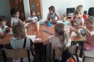 Na zdjęciu grupka dzieci pracujących w grupie przy wspólnym stole.  dzieci wykonuja prace plastyczne. 