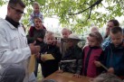 Na zdjęciu dzieci wraz z osobami dorosłymi. Jeden z chłopców ma na głowie kapelusz pszczelarski. Znajdują się wśród zieleni. 