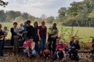 Zdjęcie grupowe osób dorosłych z dziećmi. Większość z kobiet trzyma dzieci na rękach. Widać również wózek dla dzieci. W tle jest zieleń, drzewa.