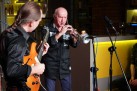 Na zdjęciu dwaj muzycy. Jeden z nich gra na gitarze, drugi na trąbce. Przed nimi dwa mikrofony. 