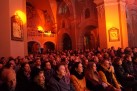 Na zdjęciu publiczność zgromadzona na koncercie. Mury kościoła oświetlone są przez lampy kolorem pomarańczowym. 