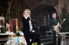 Na zdjęciu wokalistka i muzycy podczas koncertu. Widać również dekoracje bożonarodzeniowe i sprzęt muzyczny. 