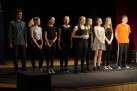 Zdjęcie grupowe aktorów występujących w spektaklu. Jedna z dziewczyn trzyma w dłoniach kwiat w doniczce. 