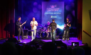 Grupa muzyczna wykonuje utwór. Scena jest oświetlona niebieskim światłem.