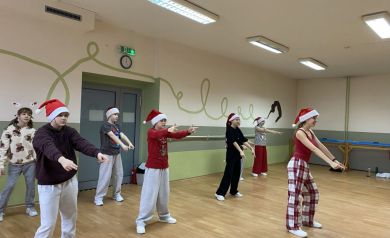 Zdjęcie przedstawia grupę młodych ludzi, dziewcząt, uczestniczących w zajęciach tanecznych w sali tanecznej. Na głowach tancerze ubrane mają czapki świąteczne. 