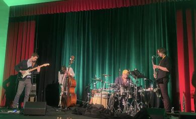 Muzycy Muizk Nva Lab na scenie, zielone oświetlenie, czerwona kurtyna 
