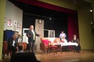 Na scenie aktorzy (dwaj mężczyźni i dwie kobiety) odgrywający scenę. Scenografia przedstawia pokój.
