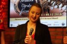 Kobieta z mikrofonem. W tle wyświetlany plakat IV Festiwalu Jazzowego. 