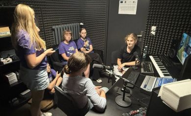 Na zdjęciu uczestnicy projektu w studio nagrań. Wokół nich wiele sprzętu muzycznego i do nagrań. - powiększ