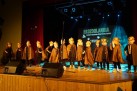 Na zdjęciu grupa przedszkolaków w takich samych przebraniach z maskami na głowach podczas występu. Przed nimi sprzęt muzyczny, zaś z tyłu widać wyświetlany plakat odbywającej się imprezy. 