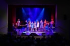 Grupa wokalistów podczas swojego występu na scenie. Na zdjęciu również część publiczności.