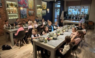 Grupa dzieci siedząca przy dwóch stołach, przed nimi składniki do robienia pizzy