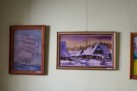 Zdjęcie przedstawia dwa obrazy w ramach wiszące na jasnej ścianie. Jeden obraz ukazuje statek, zaś drugi chatki drewniane pokryte śniegiem. 