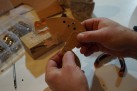 Na zdjęciu widać osobę składającą z tektury ruchomą figurkę żaby, wykorzystującą metalowe nity do połączenia elementów.