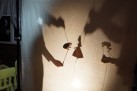 Na zdjęciu widać teatrzyk cieni — postacie księżniczek i żab z kolorowego papieru są podświetlone zza płótna, tworząc bajkową scenę w świątecznym klimacie.