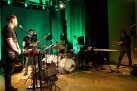 Na zdjęciu muzycy podczas swojego występu. W tle lampy oświetlające scenę na kolor zielony. 