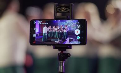Zdjęcie telefonu nagrywającego występ zespołu wokalnego. 