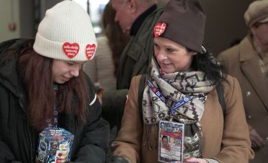 Dwie kobiety w czapkach z naklejonymi serduszkami z Wielkiej Orkiestry Świątecznej Pomocy, w rękach mają puszki z Wielkiej Orkiestry Świątecznej Pomocy. Rozmawiają. 