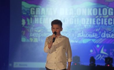 Chłopiec w białej koszuli śpiewający do mikrofonu. 