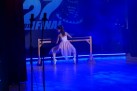 Dziewczynka w jasnej sukience podczas wykonywani układu tanecznego na scenie, którą oświetla niebieskie światło. 