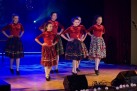 Młode dziewczyny w czerwonych sweterkach i kolorowych spódnicach tańczą na scenie. 