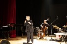 Na zdjęciu koncert Ireny Santor. Kobieta ubrana na czarno śpiewa do mikrofon. Widać również trzech mężczyzn, jeden gra na fortepianie, drugi na kontrabasie, zaś trzeci na perkusji. 