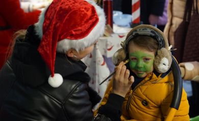 Kobieta malująca dziecko. Twarz dziecka jest zielona. 