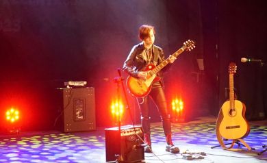 Na scenie Strzeleckiego Ośrodka Kultury, młoda dziewczyna wykonuje muzykę na gitarze. 