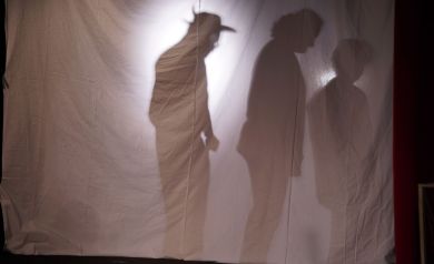 Zdjęcie przedstawia teatr cieni, na którym widoczne są sylwetki trzech osób.