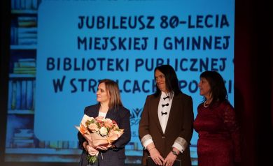 Na zdjęciu trzy kobiety. Jedna z nich trzyma w dłoni bukiet kwiatów.