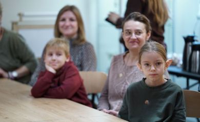 Na zdjęciu dzieci i dorośli siedzący przy stolikach.