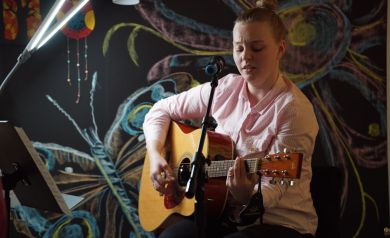 Kobieta śpiewająca i grająca na gitarze podczas występu artystycznego