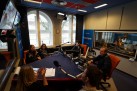 Na zdjęciu widać studio radiowe, w którym odbywa się audycja na żywo lub nagranie programu. Kilka osób siedzi przy stole z mikrofonami. Widoczne jest również logo Radia Opole.