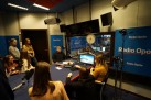 To zdjęcie przedstawia grupę młodzieży oraz osoby dorosłe w studiu radiowym, prawdopodobnie podczas nagrywania audycji lub wizyty studyjnej. Na ścianach i sprzęcie widoczne jest logo Radia Opole.