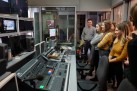 Ta grupa osób znajduje się w studio telewizyjnym. W pomieszczeniu widać stół mikserski i inne urządzenia do produkcji medialnej, co wskazuje na to, że jest to miejsce, gdzie nagrywa się programy lub audycje.