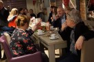 Uczestnicy wernisażu wystawy dyskutujący przy stołach. 