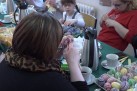Kobiety skrobiące kroszonki. Na stole nakrytym zielonym obrusem znajduje się poczęstunek i inne gotowe kolorowe kroszonki.