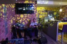 Dwóch mężczyzn grających na gitarach w klimatycznie oświetlonej restauracji. Jeden z nich śpiewa do mikrofonu. 
