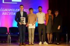 Zdjęcie pięciu osób stojących na scenie. Jeden z młodych mężczyzn trzyma w dłoniach dyplom i książkę. 