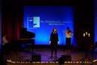 Dziewczyna występująca przy akompaniamencie fortepianu i skrzypiec. 