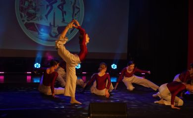 Grupa taneczna ubrana w jednakowe stroje (czerwona bluzka i jasne spodnie) podczas swojego występu. 