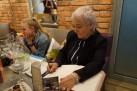 Na zdjęciu dwie kobiety. Jedna podpiera ręką głowę i patrzy przed siebie. Druga pisze coś w księdze. 