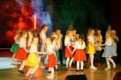 Na zdjęciu grupa dzieci podczas swojego występu. Dziewczynki ubrane są w różnokolorowe spódniczki i białe bluzki z żółtą chustą. 