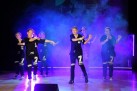 Na scenie grupa taneczna prezentująca swój występ. Scenę oświetla niebiesko-fioletowe światło i jest tam również ciężki dym. Dziewczęta ubrane są w jednakowe stroje. 