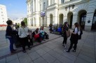 Grupa młodzieży siedząca przed białym budynkiem.