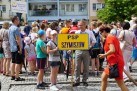 Dzieci i dorośli  zebrani na placu wśród miejskiej zabudowy. Jedna z dziewczynek trzyma tablicę z napisem PSP Szymiszów. 